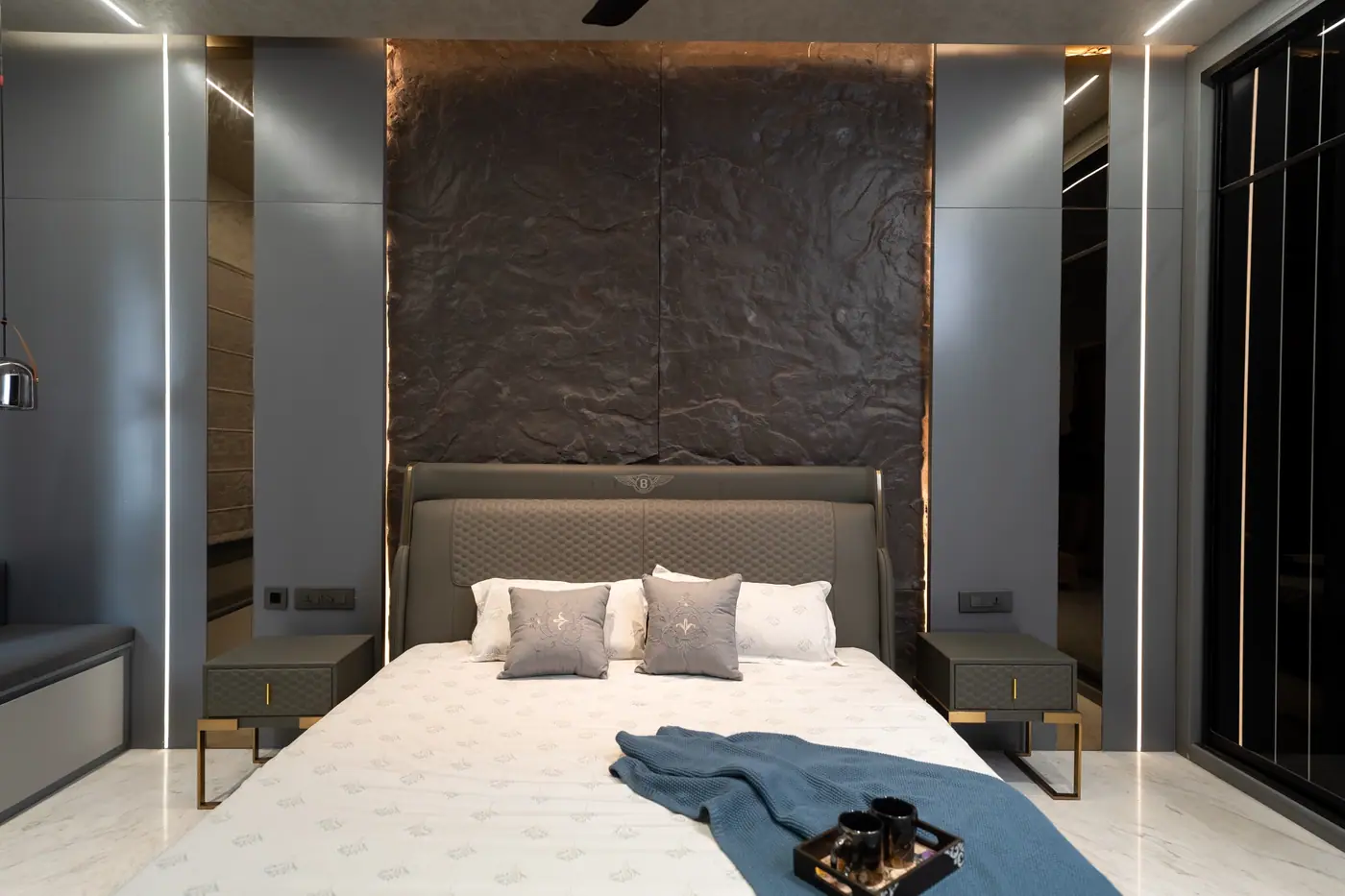 Master bedroom with a textured stone feature wall, upholstered bed and linear lighting