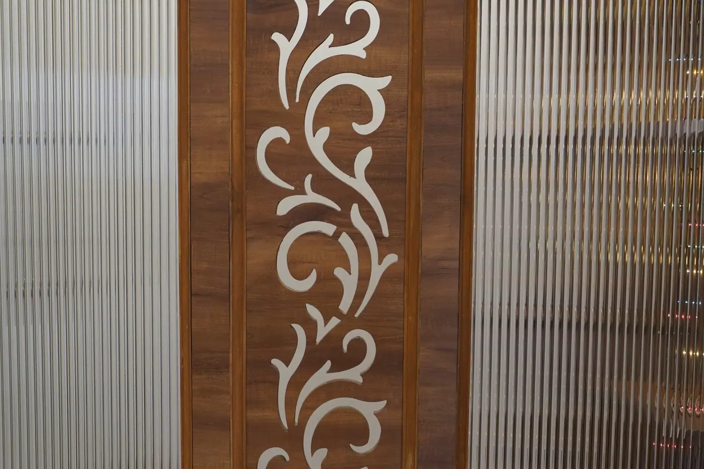 Close-up of a wood veneer panel with a white carved inlay beside fluted glass