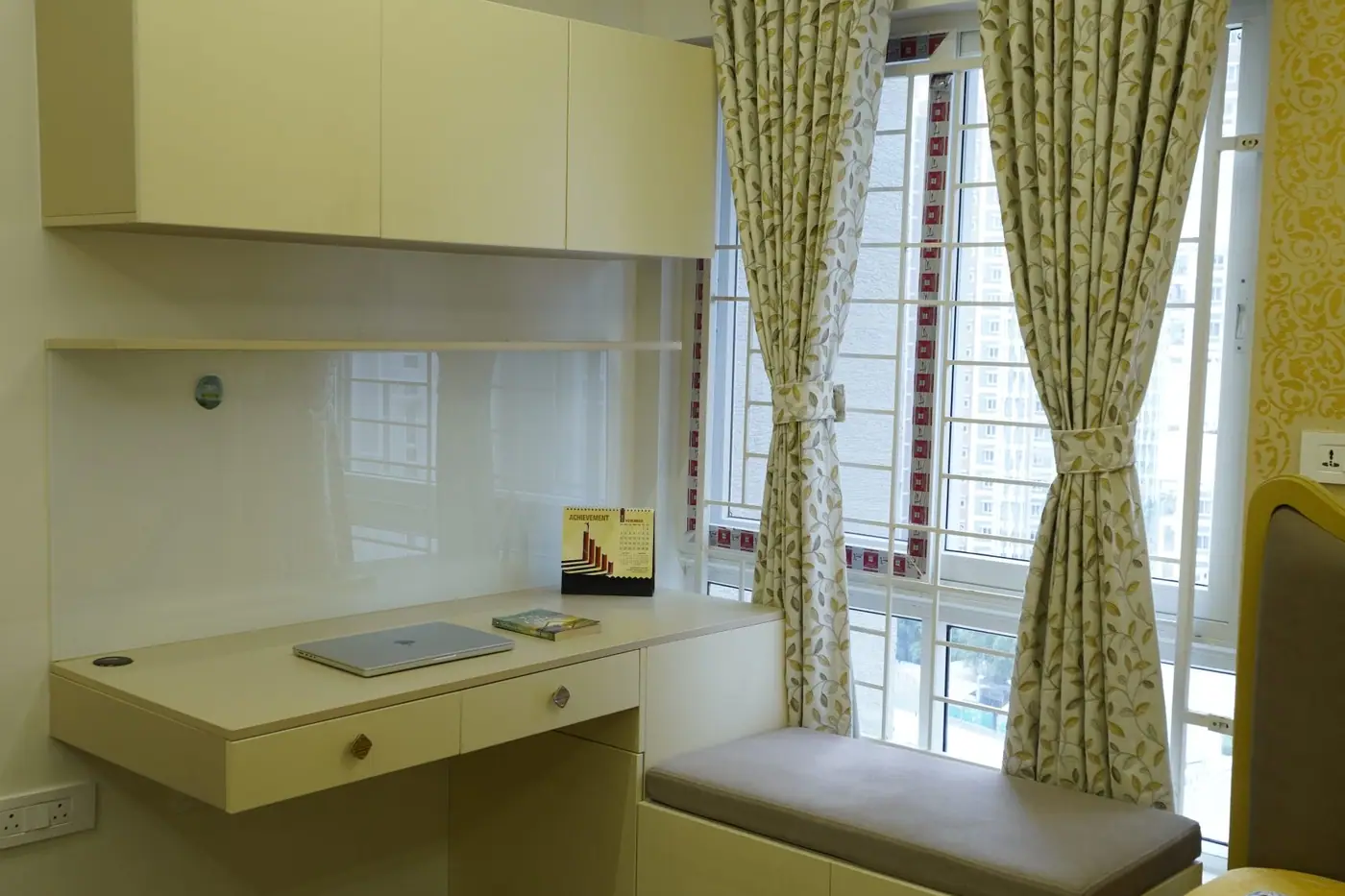 Bedroom study corner with a wall-mounted desk, overhead storage and a window seat